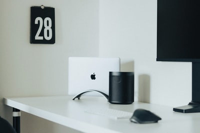 白色木质办公桌上，黑色和银色线状电脑鼠标旁的银色imac